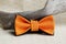 Composition: orange with a black bow tie and a wooden stick curve on a beige background.