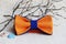 Composition: orange with a blue bow tie, colored seashells and a twig on a beige background.