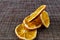 Composition of orange dried oranges slices of round shape, preserved color, on a mottled woven brown background