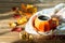 Composition with orange pumpkin styled cup of coffee and autumn themed decoration, fallen leaves, cozy scarf on brown wooden