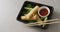 Composition of plate with spring rolls and chilli sauce with chopsticks on grey background