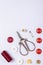 A composition of red sewing thread, thimble, vintage scissors, buttons and safety pin on a white background
