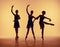 Composition from silhouettes of three young dancers in ballet poses on a orange background.