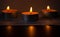 Composition of three candles on dark luxury night background. Black table, side view. Candles Burning at Night. Orange taper