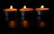 Composition of three candles on dark luxury night background. Black table, side view. Candles Burning at Night. Orange taper