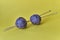 Composition of two purple balls of acrylic yarn and two wooden long spokes on yellow background.