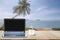 Computer laptop with black screen and hot coffee cup on wooden table top on blurred beach with coconut tree background