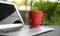 Computer laptop with offee in red cup with green nature background. Work remotely or from home