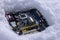 A computer motherboard with a processor lying on a dump in the snow, thrown out due to a malfunction