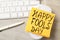 Computer mouse with Happy Fools` Day note near keyboard on wooden table, above view