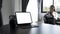 Computer tablet and coffee cup on black wooden table with businesswoman siting in background.