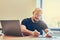 Concentrated adult bald man manager using laptop while writing notes in notebook at workplace.