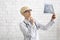 Concentrated adult female doctor in glasses and white coat looks at x-ray jaw on white brick wall background