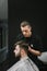 Concentrated barber cuts the client`s scissors in a dark barber shop. Male hairdresser creates a stylish hairstyle for a bearded