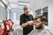 Concentrated barber makes hair bearded client in a modern light barber shop, uses a clipper. Male hairdresser prepares hairstyle