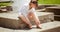 Concentrated beautiful  little girl sitting on concrete blocks in outdoor park and adjusting, fixing her shoe belt