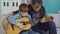 Concentrated child is playing guitar with his father experienced guitarist, adjusting musical instrument and enjoying