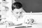 Concentrated cute child, writing in notebook using pencil. Cute child is sitting at a desk indoors.