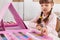Concentrated diligent little girl drawing at home while sitting at table, kid choosing wax crayons for painting picture, child
