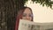 Concentrated elegant lady reading newspaper in park. Focused young female entrepreneur with long dye hair in formal wear