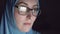 Concentrated face of Muslim woman in hijab and glasses at night in the dark searches the Internet