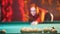 Concentrated ginger woman playing billiard in billiard club. Breaks down arranged balls