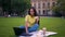 Concentrated girl is having lunch in the park. Girl works on laptop and eats a sandwich. 4K