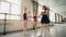 Concentrated girls are learning basic ballet positions in dancing school with careful teacher helping them to master
