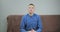 Concentrated guy in blue shirt talks sitting on brown sofa