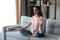 Concentrated indian female sitting on sofa practicing yoga pranayama exercises