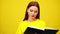 Concentrated intelligent millennial woman reading book at yellow background and smiling. Portrait of confident smart