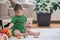 Concentrated little boy examining colorful toys sitting on fluffy rug against houseplant