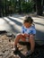 A concentrated little girl with a scratched knee sits on the asphalt in the summer
