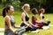 Concentrated multinational ladies meditating or doing breathing exercises on yoga practice outside, empty space