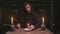 Concentrated mysterious wizard male fortune teller lights a red candle and puts it on plate