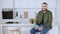 Concentrated positive man sitting in kitchen using tablet and looking at camera smiling. Portrait of handsome confident