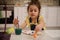 Concentrated preschooler cute little European girl enjoys painting while sitting at wooden table, mixing watercolors paints or