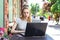 A concentrated Self employed Caucasian woman working with her phone and laptop in a restaurant terrace