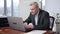 Concentrated senior Caucasian man sitting in office working online on laptop. Portrait of confident focused employee