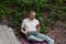 Concentrated serious man startup entrepreneur with laptop and phone sits outdoors near brick wall