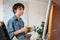 Concentrated short-haired female artist painting on cotton canvas with oil paint at home