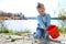 Concentrated toddler playing with his toy bucket and shovel near the river. Springtime. Investigate  details of nature. outdoor