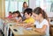 Concentrated tween girl listening to schoolteacher and writing in notebook