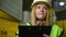 Concentrated woman in hard hat thinking writing in documents standing in warehouse. Portrait of focused female Caucasian