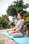 Concentrated woman sitting in lotus position yoga at summer garden park plants and blossom flowers