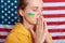 Concentrated woman wearing yellow hoodie and with flag of Ukraine on her cheek, isolated over USA flag, keeping hands in pray