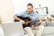 Concentrated young man at home with laptop playing guitar