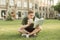Concentrating young man in casual clothing reads a book and is eating a sandy sitting on the lawn. Student street portrait dishes