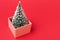 Concept of an approaching holiday, a Christmas tree sticks out of a gift box, on a red background