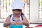 Concept of Asian girl learning to cook or snack. Child wearing glasses is hammering the egg into the blue-white bowl.